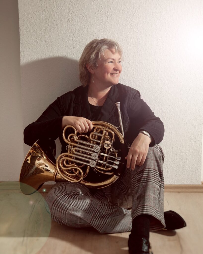 Isabelle Van de Wiele sitzt mit ihrem Horn auf dem Boden und lächelt