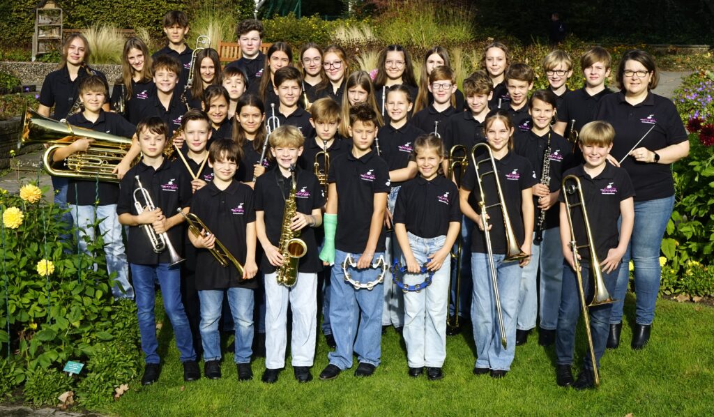 Gruppenfoto des sjb Nachwuchs-Orchesters mit Instrumenten auf einer Wiese, rechts Dirigentin Dorothee Wember