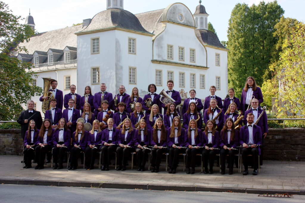 Gruppenfoto des Schönebecker Jugend-Blasorchesters in lila Uniformjacken mit Instrumenten vor Schloss Borbeck